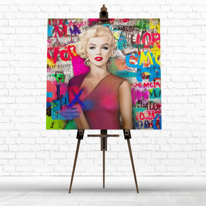 Colorful artwork of a marilyn monroe wearing a pink dress with graffiti letters on an easel against a white brick wall.